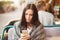 Photo of serious brunette young lady uses new cell phone for chatting and communication, waits for order in outside cafeteria,