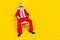 Photo of serious confident man pensioner dressed red suit santa hat sitting chair empty space isolated yellow color