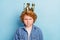 Photo of serious grumpy ginger kid look camera wear golden crown denim jacket isolated blue color background