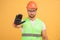 Photo of serious stern unshaven builder shows stop gesture, wears orange protective construction helmet, reflective waistcoat,