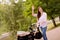 Photo of shiny excited mother dressed casual clothes walking buggy little son waving arm hi outdoors backyard