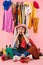 Photo of shocked young woman wearing hat sitting near bunch of clothes