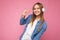 Photo shot of beautiful positive smiling young blonde woman wearing white wireless bluetooth headsets listening to cool