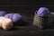 This photo shows a wicker basket with purple yarn and skeins of wool on a dark wooden background.