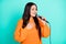 Photo of singer lady hold microphone hand chest open mouth wear orange pullover  teal color background