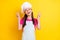 Photo of small excited friendly lady show two v-signs wear white apron hat isolated yellow color background