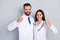 Photo of smart happy two docs dressed white coats embracing showing thumbs up  grey color background