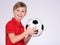 Photo of a smiling boy in sportswear holding soccer ball, posing at studio. Happy 8 years old kid in a red t-shirt with a soccer