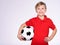 Photo of a smiling boy in sportswear holding soccer ball, posing at studio. Happy 8 years old kid in a red t-shirt with a soccer