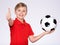 Photo of a smiling boy in sportswear holding soccer ball, posing at studio. Happy 8 years old kid in a red t-shirt with a soccer