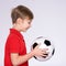 Photo of a smiling boy in sportswear holding soccer ball, posing at studio. Profile portrait of a happy 8 years old kid in a red t