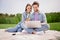 Photo of smiling lovely couple sit outside in park husband browsing in laptop wife point finger buy online shopping sale