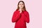 Photo of spiritual woman keeps eyes closed, hands in praying gesture, dressed in red outfit, prays for good wellness, poses over