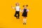 Photo of sporty cheerful kids jump hold hands show v-sign wear school uniform  yellow color background
