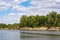 Photo of a steep river Bank on a bright Sunny day against a cloudy sky. The sandy beach is overgrown with poplars