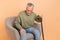 Photo of stressed elder grey hairdo man sit with stick wear pullover jeans  on beige background