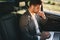 Photo of successful man wearing suit and bluetooth earphones working on laptop, while back sitting in business class car