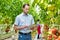 Photo of supervisor checking tomatoes while writing report in greenhouse