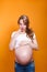 Photo of surprised emotional pregnant woman standing over yellow background.