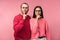 Photo of sweet couple in glasses stands and shows shhh. Male and female look serious and strict, isolated over pink