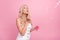 Photo of sweet pretty young lady wear white overall blowing soap bubbles  pink color background
