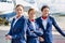 Photo of three confident flight attendants standing against airplane in airport