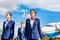 Photo of three confident flight attendants walking against airplane in airport