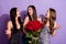 Photo of three funny ladies hold roses share rumors laugh wear glossy dresses isolated purple color background