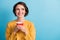 Photo of toothy beaming lady wearing casual yellow sweater holding cup hands arms looking empty space isolated blue