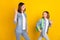 Photo of two cute friendly sisters wear jeans shirts smiling saying goodbye waving arms isolated yellow color background