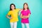 Photo of two funny white friendly kind nice cute girls wearing yellow and pink t-shirts while isolated with teal