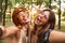 Photo of two joyful hippie women, smiling and taking selfie while walking in forest