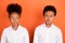 Photo of two young preteen black kids unhappy upset suspicious think isolated over orange color background