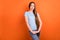 Photo of unsure brown hairdo young lady hold hands look empty space wear blue t-shirt isolated on vivid orange color