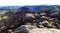 A photo of vegetation being harmed by fire damage, mountain rocks, burnt bushes and a mountain range in the distance