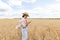 Photo of woman in straw hat looking on cellphone while walking on wheat field at summer day