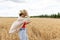 Photo of woman in straw hat looking on cellphone while walking on wheat field at summer day