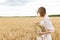 Photo of woman in straw hat looking on cellphone while walking on wheat field at summer day