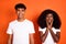 Photo of young afro couple boyfriend smiling and unhappy girlfriend hold hands cheeks isolated on orange color