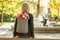 Photo of young blonde dreamy woman with bouquet of flowers in grey backpack in a spring summer park