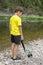 Photo of young boy standing back to front and dropping camera on stones of stream.