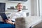 Photo of young brunet looking to side with tablet in his hands sitting on sofa in room.