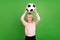 Photo of young cheerful charming boy hold hands football above head isolated on green color background