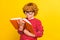Photo of young focused serious redhead boy look hold hands book reader  on yellow color background
