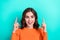 Photo of young funny overjoyed brown curly hair lady wear orange shirt surprised directing fingers up mockup isolated on