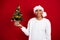 Photo of young funny saint nicholas guy wear white pullover hold evergreen little christmas tree with adornment isolated