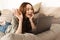 Photo of young happy woman with brown hair lying on sofa in living room, and looking on camera of laptop while speaking on video