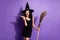 Photo of young lovely smiling amazed surprised witch girl holding broomstick isolated on violet color background