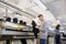 Photo of a young man analysing a piece of clothes and a woman working on industrial knitting machine