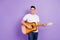 Photo of young man happy positive smile look empty space play guitar artist concert isolated over violet color